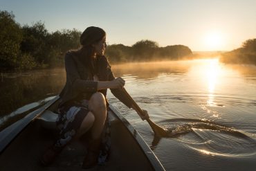 Balade en canoë au lever du soleil en Bretagne avec une participante pagayant sur une rivière entourée de nature à La Gacilly – Destination Yves Rocher