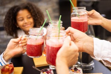 Moment convivial en Bretagne avec participants trinquant des smoothies maison autour d’une table, ambiance familiale et gourmande – Destination Yves Rocher