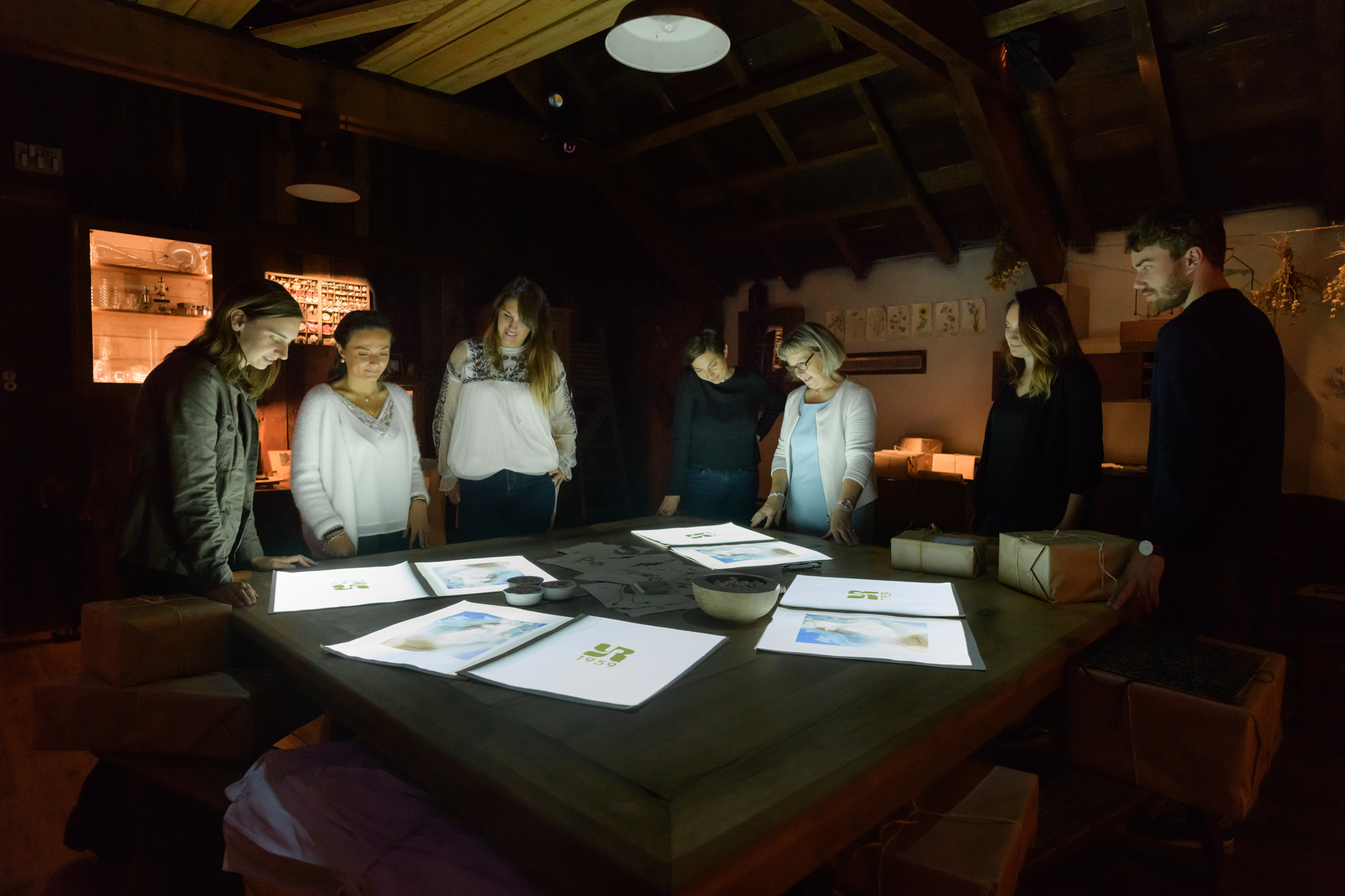 Atelier immersif en Bretagne avec un groupe de participants observant des supports lumineux autour d’une grande table dans une ambiance intimiste à La Gacilly – Destination Yves Rocher