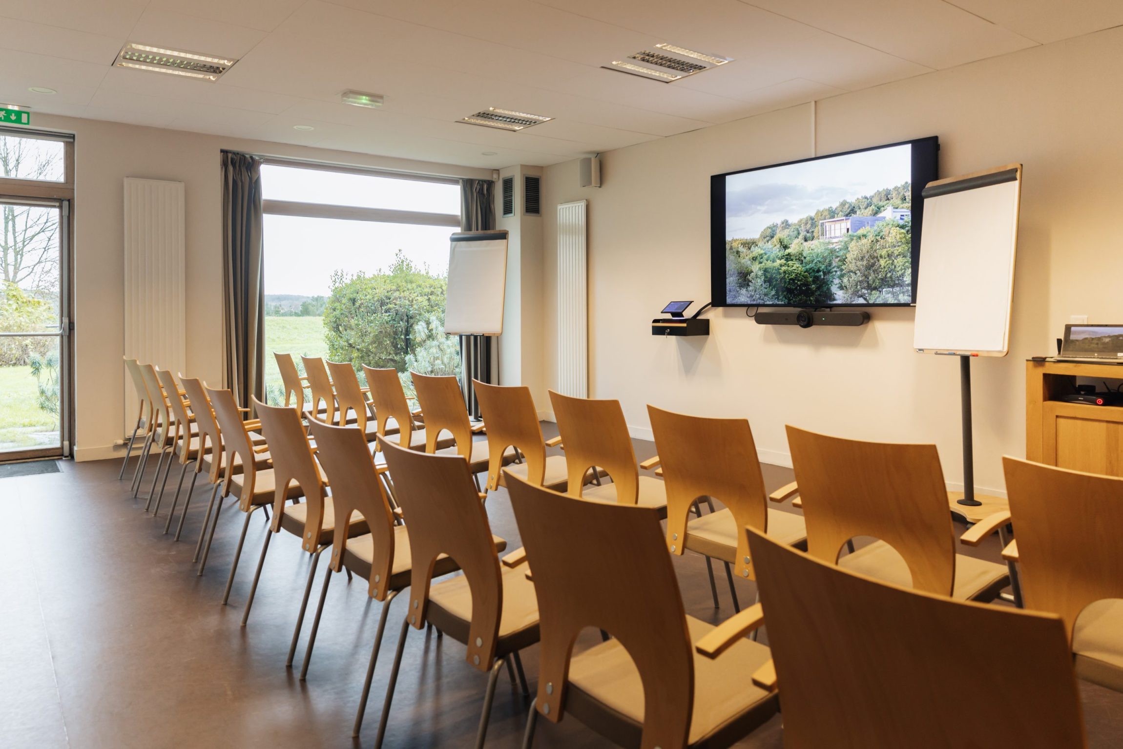 Salle de séminaire moderne en Bretagne avec rangées de chaises, écran de présentation et vue sur la nature, espace idéal pour réunions professionnelles – Destination Yves Rocher